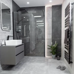 Moderná šedá kúpeľňa s walk-in sprchou za sklom, závesnou skrinkou s umývadlom, čiernymi batériami a čiernym rebríkovým radiátorom