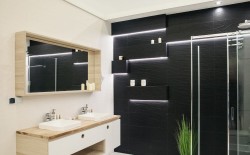Čierna akcentná stena so zapustenými policami a LED linkami, vedľa sprchovací kút; umývadlá pod zrkadlovou skrinkou