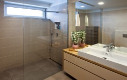 Kúpeľňa s priestranným sprchovacím kútom a širokým umývadlom, závesné svietidlá nad doskou a veľké zrkadlo odrážajúce svetlo do miestnosti