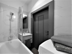 Paneláková kúpeľňa s vaňou a umývadlom; biele mramorové obklady a kontrastné tmavé dvere