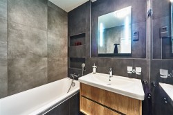 Kúpeľňa s obmurovanou vaňou, podsvieteným zrkadlom a umývadlom na drevenej skrinke; tmavé betónové obklady a nika na kozmetiku v stene