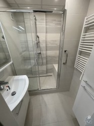 Úzka svetlá kúpeľňa so sprchovacím kútom s posuvnými dverami, rebríkovým radiátorom a malým umývadlom na skrinke