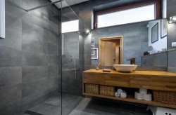 Šedá kúpeľňa s veľkou sprchou so sklenenou zástenou, masívnou drevenou umývadlovou doskou s miskovým umývadlom a úložnými košmi v spodnej polici