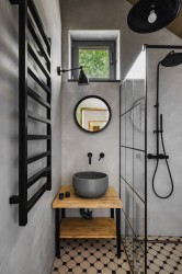 Úzka kúpeľňa so šedou stierkou, čiernym rebríkovým radiátorom, umývadlom na drevenej otvorenej skrinke a sprchovacím kútom s čiernymi prvkami