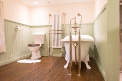 Elegantná retro kúpeľňa s vaňou na nôžkach, vysokou stojanovou batériou, drevenou podlahou a svetlým obkladom