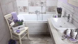 Útulná kúpeľňa s vaňou, bielym umývadlom, drevenou stoličkou a levanduľovými dekoráciami v jemných krémových odtieňoch