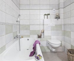 Menšia kúpeľňa s vaňou, závesným WC, svetlým obkladom a levanduľovými doplnkami v provence štýlu