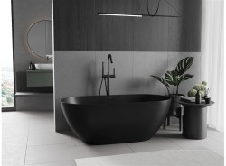 Dominantná matne čierna voľne stojaca vaňa pred šedými obkladmi, minimalistická čierna batéria a prírodná dekorácia na okrúhlom odkladacom stolíku