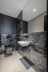 Moderná toaleta s kompaktným umývadlom, kontrast svetlej podlahy a tmavého kamenného obkladu