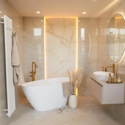 Voľne stojaca vaňa v béžovej kúpeľni, zlatá stojanková batéria a podsvietený mramorový panel ako dominantný prvok steny