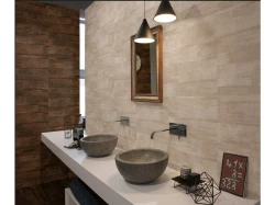 Dvojica kamenných miskových umývadiel na bielej doske, nástenné batérie a drevený rám zrkadla v teplom hnedobéžovom ladení