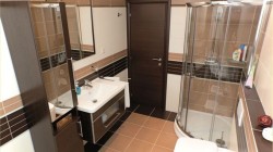 Kúpeľňa s rohovým sprchovacím kútom, bielym umývadlom na skrinke a vodorovnými pruhmi obkladov v bielej, béžovej a tmavo hnedej