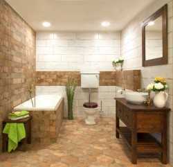 Kúpeľňa s obmurovanou vaňou, dlažbou v kamennom vzhľade, drevenou skrinkou s miskovým umývadlom a batériami v mosadze