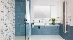 Moderná modrá kúpeľňa s walk-in sprchou, bielym závesným pultom s hranatým umývadlom a veľkým zrkadlom