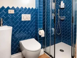 Malá kúpeľňa s modrým obkladom vo vzore rybej kosti, závesným WC a sprchovacím kútom s čiernymi profilmi a posuvnými dverami