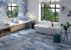 Priestranná kúpeľňa s modrobielym mramorovým dekorom na stenách i podlahe, voľne stojacou vaňou, dvojitým umývadlom a zlatými batériami