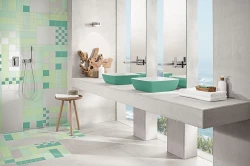 Svetlá kúpeľňa s mozaikou v zelených tónoch, dvoma tyrkysovými umývadlami na betónovej doske a sprchou s podomietkovou batériou