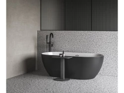 Matne čierna voľne stojaca vaňa na terrazzo podlahe, čierna stojanková batéria a šedé steny v minimalistickom prevedení