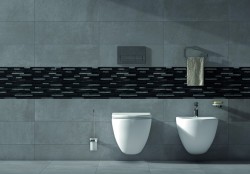 Detail závesného WC a bidetu na šedých obkladoch s čiernym mozaikovým pruhom a doplnkami v chróme