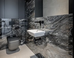 Malá čiernosivá toaleta s výrazným mramorovým dekorom, závesným umývadlom, čiernou podomietkovou batériou a WC v tmavom prevedení