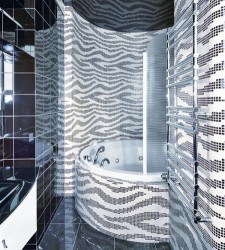 Šedobiela kúpeľňa s výraznou „zebra“ mozaikou na stenách a obmurovanou rohovou vaňou; chrómový rebríkový radiátor v popredí