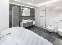 Elegantná kúpeľňa so šedým obkladom v dekore dreva, umývadlom na skrinke, podsvieteným zrkadlom a závesným wc a bidetom