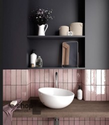 Detail umývadlového kútika: biele asymetrické umývadlo na drevenej doske, lesklé ružové obklady „tehličky“ a otvorené police s doplnkami