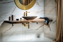 Detail kamenného umývadla na doske; zlatý sifón aj batérie a okrúhle zrkadlo v zlatom ráme na mramorovom obklade