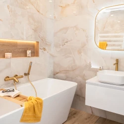 Kúpeľňa so vstavanou vaňou, nikou s podsvietením a drevodekorom, zlatou vaňovou batériou a bielym umývadlom na závesnej skrinke