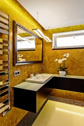 Kúpeľňa so zlatou stierkou na stenách, čiernou rohovou skrinkou, bielym umývadlom a veľkým zrkadlom v dekoratívnom ráme