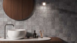 Detail umývadlovej zóny: biele umývadlo na doske, veľké kruhové zrkadlo a mozaikový obklad v šedom kamennom vzhľade