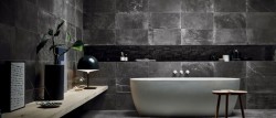 Tmavá kúpeľňa s veľkoformátovým betónovým obkladom, bielou voľne stojacou vaňou a minimalistickými doplnkami v čiernej farbe