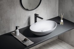 Detail umývadlovej zóny s oválnym bielym umývadlom, čiernou batériou a stierkou v jemnom betónovom dekore