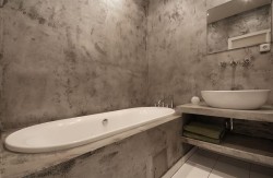 Malá kúpeľňa so vstavanou vaňou, otvorenou policou pod umývadlom a stenami v surovom betónovom vzhľade