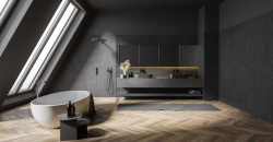 Minimalistická podkrovná kúpeľňa s tmavými obkladmi, voľne stojaca oválnou vaňou pri strešnom okne a dlhou skrinkou s dvoma umývadlami