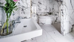Kúpeľňa s bielym mramorovým obkladom, hranatým umývadlom s dvoma batériami a rohovou vaňou