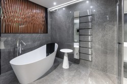 Šedá kúpeľňa s mramorovým dekorom, voľne stojaca minimalistickou vaňou, vysokým chrómovým radiátorom a dekoratívne panely na stene