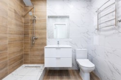 Svetlá klasická kúpeľňa s bielym nábytkom, sprchovacím kútom v drevodekore a chrómovaným kúpeľňovým rebríkom na mramorovom obklade